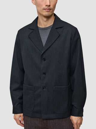 Atelier-Overshirt in Dunkelblau mit gekerbtem Kragen, drei Knöpfen und zwei aufgesetzten Vordertaschen, getragen über einem grauen Hemd.