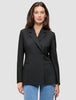 Eine Person, die einen schwarzen Avira-Blazer für Damen mit fallendem Revers und eine blaue Jeans trägt, die das minimalistische skandinavische Design unterstreichen.
