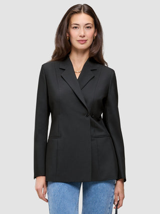 Eine Person, die einen schwarzen Avira-Blazer für Damen mit fallendem Revers und eine blaue Jeans trägt, die das minimalistische skandinavische Design unterstreichen.