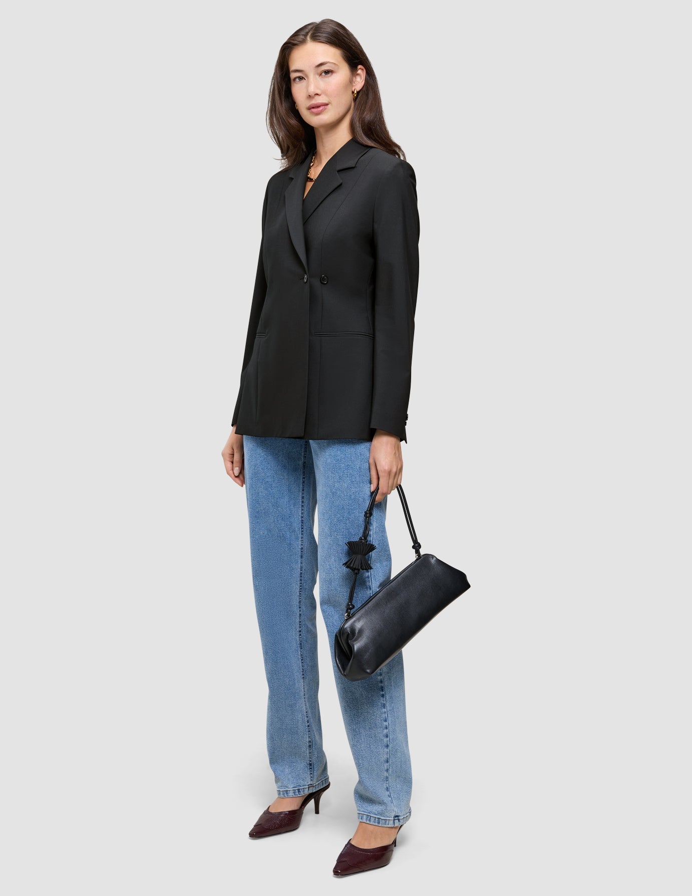 Eine Frau trägt einen schwarzen, zweireihigen Avira Blazer Black-Damenblazer zu einer blauen Jeans und hat eine schwarze Handtasche dabei.