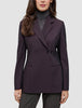 Eine Frau trägt einen dunkelvioletten Women’s Avira Blazer Burgundy Berry im klassischen skandinavischen Zweireiher-Design über einem grauen Rollkragenpullover.