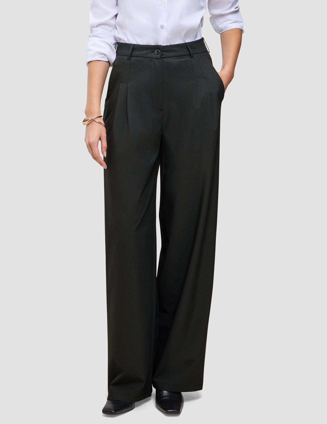 Die Damenhose Avira Pants Wide in Schwarz mit hoher Taille und weitem Bein, kombiniert mit einem weißen Hemd, das in die Hose gesteckt wurde.
