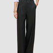 Die Damenhose Avira Pants Wide in Schwarz mit hoher Taille und weitem Bein, kombiniert mit einem weißen Hemd, das in die Hose gesteckt wurde.