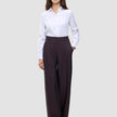 Eine Person, die ein weißes, langärmeliges Hemd mit Knöpfen trägt, das in die Damenhose Avira Pants Wide in der Farbe Burgundy Berry gesteckt ist.