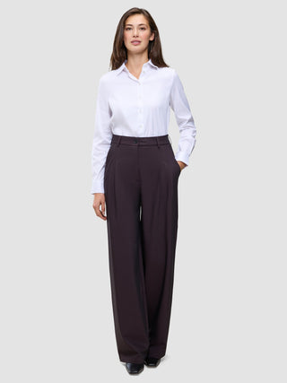 Eine Person, die ein weißes, langärmeliges Hemd mit Knöpfen trägt, das in die Damenhose Avira Pants Wide in der Farbe Burgundy Berry gesteckt ist.