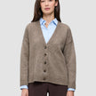 Ein Model trägt eine Damen-Strickjacke aus weicher, grobstrickiger Wolle in Taupe-Melange über einem hellblauen Hemd mit Kragen.