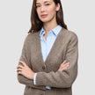 Eine Frau, die eine Damen-Strickjacke aus weicher, grobstrickiger Wolle in Taupe-Melange über einem hellblauen Hemd mit Kragen trägt.