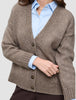Eine grob gestrickte, weiche Wollstrickjacke für Damen in Taupe-Melange, über einem hellblauen Hemd mit Kragen geknöpft.
