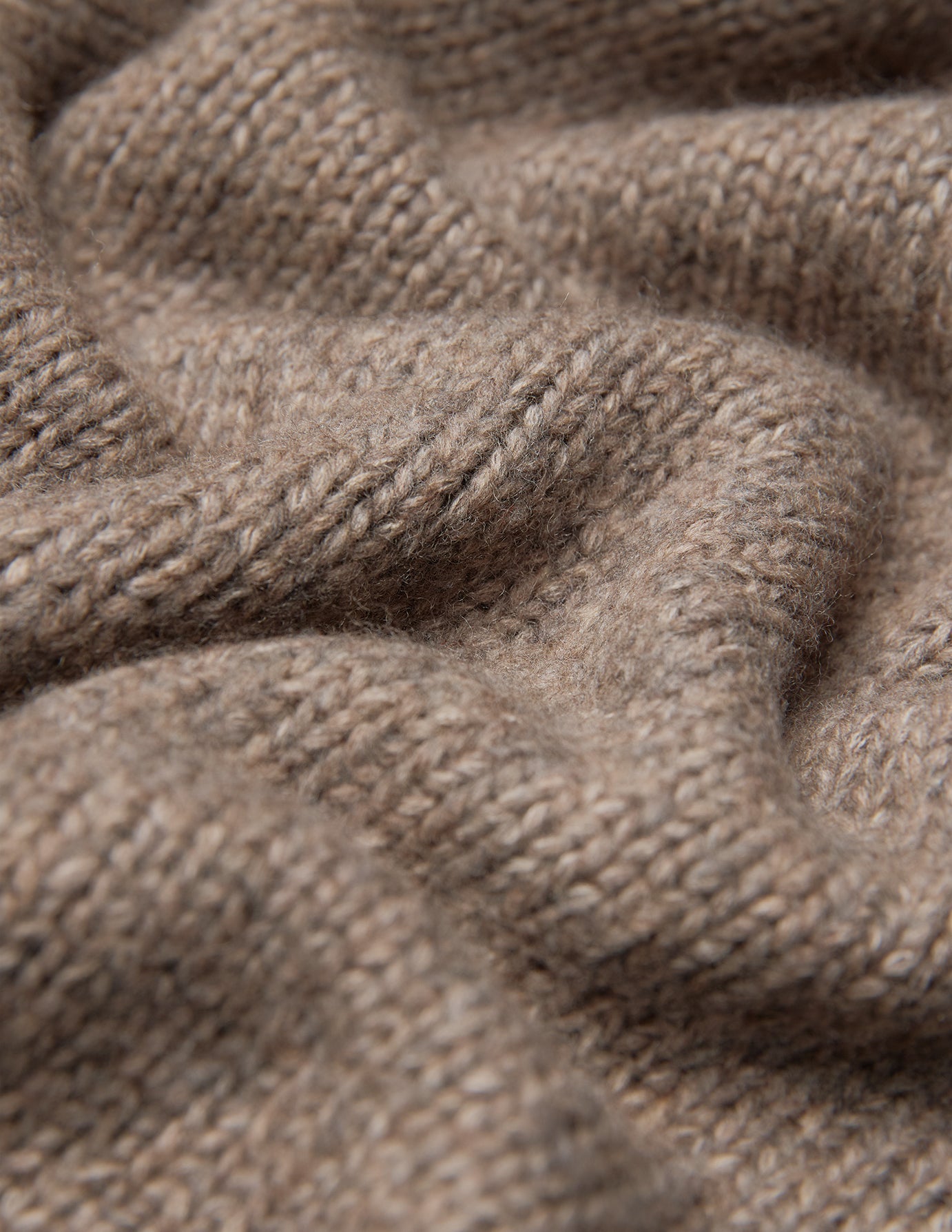 Nahaufnahme einer Damen-Strickjacke aus weicher, grobstrickiger Wolle in Taupe-Melange, die sich durch eine dicke, taupefarbene Grobstrick-Struktur aus Merinowolle auszeichnet.