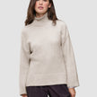 Eine Frau, die einen beigen Damen-Rollkragenpullover aus grobem, weichem Wollstrick in der Farbe Sugar Melange trägt, dazu eine dunkle Hose.