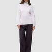 Eine Frau, die einen Damen-Rollkragenpullover aus dicker, weicher Wolle in der Farbe Sugar Melange in Off-White und eine dunkle Hose mit weitem Bein trägt.