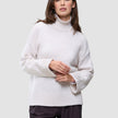 Eine Frau, die einen cremefarbenen Damen-Rollkragenpullover aus dickem, weichem Wollstrick in der Farbe Sugar Melange mit weiten Ärmeln trägt.