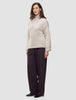 Eine Frau, die einen beigen Damen-Rollkragenpullover aus dickem, weichem Wollstrick in der Farbe Sugar Melange und eine dunkle Hose mit weitem Bein trägt.