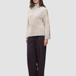 Eine Frau, die einen beigen Damen-Rollkragenpullover aus dickem, weichem Wollstrick in der Farbe Sugar Melange und eine dunkle Hose mit weitem Bein trägt.