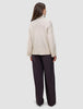 Eine Person, von hinten gesehen, die einen cremefarbenen, dicken, weichen Damen-Rollkragenpullover aus Wolle in der Farbe Sugar Melange sowie eine dunkle Hose mit weitem Bein trägt.