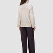 Eine Person, von hinten gesehen, die einen cremefarbenen, dicken, weichen Damen-Rollkragenpullover aus Wolle in der Farbe Sugar Melange sowie eine dunkle Hose mit weitem Bein trägt.