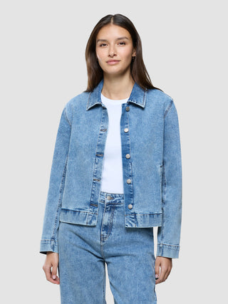 Eine Frau, die ein weißes T-Shirt und eine „Women’s Classic Denim Jacket Snow Blue Wash“ sowie dazu passende Jeans trägt.