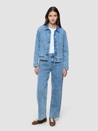 Eine Frau, die ein weißes T-Shirt, eine klassische Damen-Jeansjacke in der Farbe „Snow Blue Wash“ und dazu passende, locker sitzende Jeans trägt.