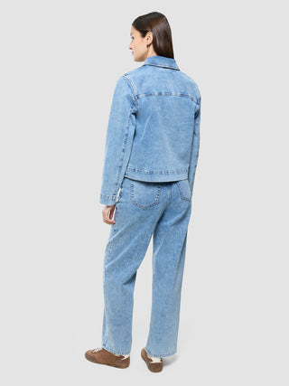 Eine Frau, von hinten gesehen, die eine „Women’s Classic Denim Jacket“ in der Farbe „Snow Blue Wash“ sowie dazu passende Jeans und braune Sneaker trägt.