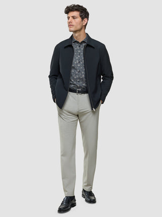 Ein Mann, der eine schwarze Jacke mit Reißverschluss über einem grauen Classic-Hemd mit Blumenmuster in Regular-Passform, eine hellgraue Hose und schwarze Loafer trägt.