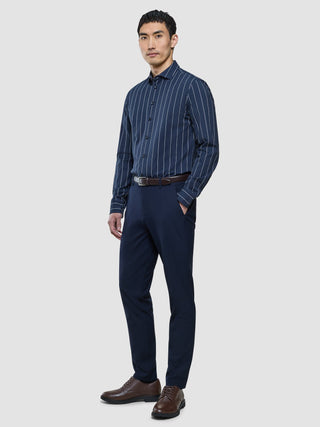 Ein Mann, der ein „Classic Shirt Midnight Pinstripes Regular“, eine marineblaue Anzughose, einen braunen Gürtel und braune Anzugschuhe trägt.