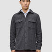 Ein Mann trägt ein doppellagiges Woll-Overshirt in der Farbe Regular Dark Grey über einem weißen Hemd mit Kragen, das ein minimalistisches skandinavisches Design widerspiegelt.