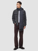 Ein Mann, der ein doppellagiges Woll-Overshirt in Regular-Passform und Dunkelgrau über einem weißen Hemd trägt, dazu eine dunkle Hose, dunkle Slipper und einen langen grauen Schal.