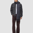 Ein Mann, der ein doppellagiges Woll-Overshirt in Regular-Passform und Dunkelgrau über einem weißen Hemd trägt, dazu eine dunkle Hose, dunkle Slipper und einen langen grauen Schal.
