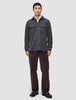 Ein Mann trägt ein doppellagiges Woll-Overshirt in Regular-Passform in Dunkelgrau über einem weißen Hemd, dazu eine dunkle Hose und schwarze Loafer im skandinavischen Design.