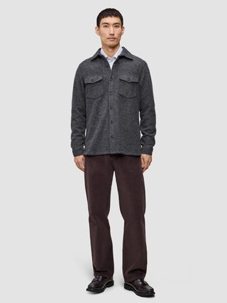 Ein Mann trägt ein doppellagiges Woll-Overshirt in Regular-Passform in Dunkelgrau über einem weißen Hemd, dazu eine dunkle Hose und schwarze Loafer im skandinavischen Design.