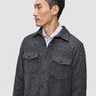 Ein Mann, der ein doppellagiges Woll-Overshirt in der Farbe Regular Dark Grey über einem Hemd mit Kragen trägt, das sich durch ein klares, skandinavisches Design auszeichnet.