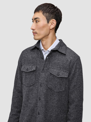 Ein Mann, der ein doppellagiges Woll-Overshirt in der Farbe Regular Dark Grey über einem Hemd mit Kragen trägt, das sich durch ein klares, skandinavisches Design auszeichnet.
