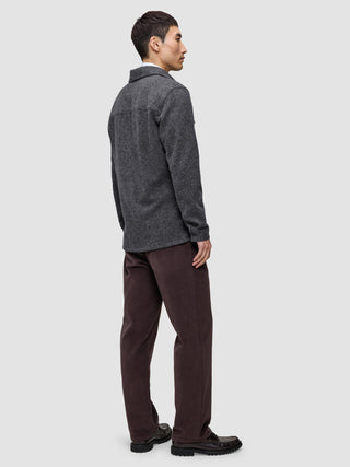 Eine Person, von hinten gesehen, die ein doppellagiges Woll-Overshirt in der Ausführung Regular in Dunkelgrau, eine dunkelbraune Hose und schwarze Slipper trägt.