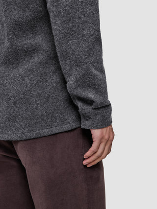 Nahaufnahme einer Person, die ein dunkelgraues, doppellagiges Woll-Overshirt in regulärer Passform mit geknöpften Manschetten trägt, kombiniert mit einer braunen Hose.