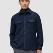 Eine Person, die ein doppellagiges Woll-Overshirt in der Farbe Regular Dark Navy über einem dunkelbraunen Rollkragenpullover trägt und damit klassisches skandinavisches Design zur Geltung bringt.