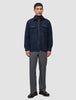 Eine Person trägt ein doppellagiges Woll-Overshirt in der Farbe Regular Dark Navy über einem braunen Rollkragenpullover, dazu eine graue Hose und dunkle Leder-Loafer.