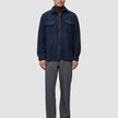 Eine Person trägt ein doppellagiges Woll-Overshirt in der Farbe Regular Dark Navy über einem braunen Rollkragenpullover, dazu eine graue Hose und dunkle Leder-Loafer.