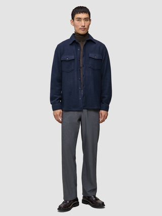 Eine Person trägt ein doppellagiges Woll-Overshirt in der Farbe Regular Dark Navy über einem braunen Rollkragenpullover, dazu eine graue Hose und dunkle Leder-Loafer.