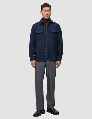 Eine Person trägt ein doppellagiges Woll-Overshirt in der Farbe Regular Dark Navy über einem braunen Rollkragenpullover, dazu eine graue Hose und dunkle Leder-Loafer.
