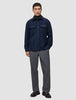 Ein Mann trägt ein doppellagiges Wollhemd in der Farbe Regular Dark Navy über einem dunklen Rollkragenpullover, dazu eine graue Hose und dunkle Leder-Loafer im minimalistischen skandinavischen Design.