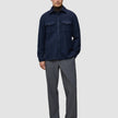Ein Mann trägt ein doppellagiges Wollhemd in der Farbe Regular Dark Navy über einem dunklen Rollkragenpullover, dazu eine graue Hose und dunkle Leder-Loafer im minimalistischen skandinavischen Design.