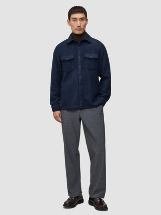 Ein Mann trägt ein doppellagiges Wollhemd in der Farbe Regular Dark Navy über einem dunklen Rollkragenpullover, dazu eine graue Hose und dunkle Leder-Loafer im minimalistischen skandinavischen Design.