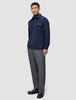 Ein Mann, der ein doppellagiges Wollhemd in der Farbe Regular Dark Navy über einem braunen Rollkragenpullover trägt, dazu eine graue Hose und dunkle Slipper.
