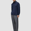 Ein Mann, der ein doppellagiges Wollhemd in der Farbe Regular Dark Navy über einem braunen Rollkragenpullover trägt, dazu eine graue Hose und dunkle Slipper.