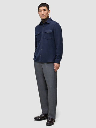 Ein Mann, der ein doppellagiges Wollhemd in der Farbe Regular Dark Navy über einem braunen Rollkragenpullover trägt, dazu eine graue Hose und dunkle Slipper.