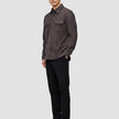 Eine Person, die ein doppellagiges Woll-Overshirt in Sattelbraun mit Brusttaschen, eine schwarze Hose und schwarze Loafer trägt.