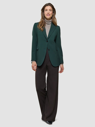 Eine Frau, die einen „Women Ease Blazer Evergreen“, einen beigen Rollkragenpullover und eine dunkle Hose mit weitem Bein trägt.
