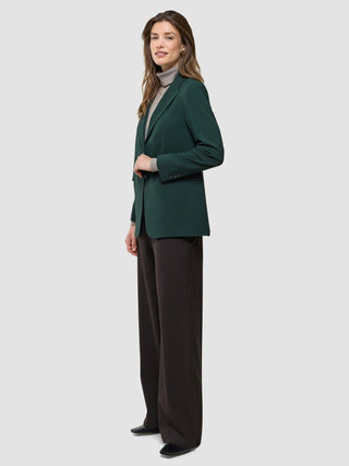 Eine Frau im Profil, die einen „Women Ease Blazer Evergreen“ über einem grauen Rollkragenpullover und einer dunklen Hose trägt.