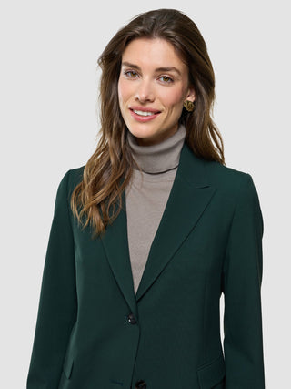 Eine lächelnde Frau, die einen „Women Ease Blazer Evergreen“ über einem grauen Rollkragenpullover trägt.