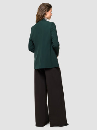 Eine Frau, die mit dem Rücken zur Kamera steht und einen „Women Ease Blazer Evergreen“ über einer schwarzen Hose mit weitem Bein trägt.